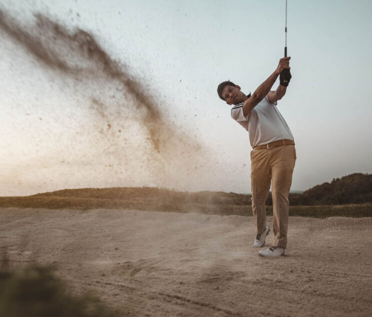 lifestyle, golf, activity, sport, golfer concept A man is sweeping golf on the sand with a beautiful posture at a golf course to practice golfing skills professionally at sunset in the summer. Sport lifestyle concept.