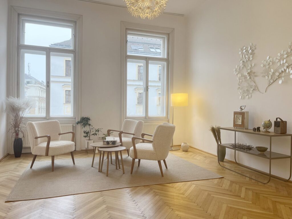Wartebereich der Praxis Las Almas in der Stiftgasse 21, Wien: Altbau mit Parkett, hohen Fenstern und weißen Sesseln